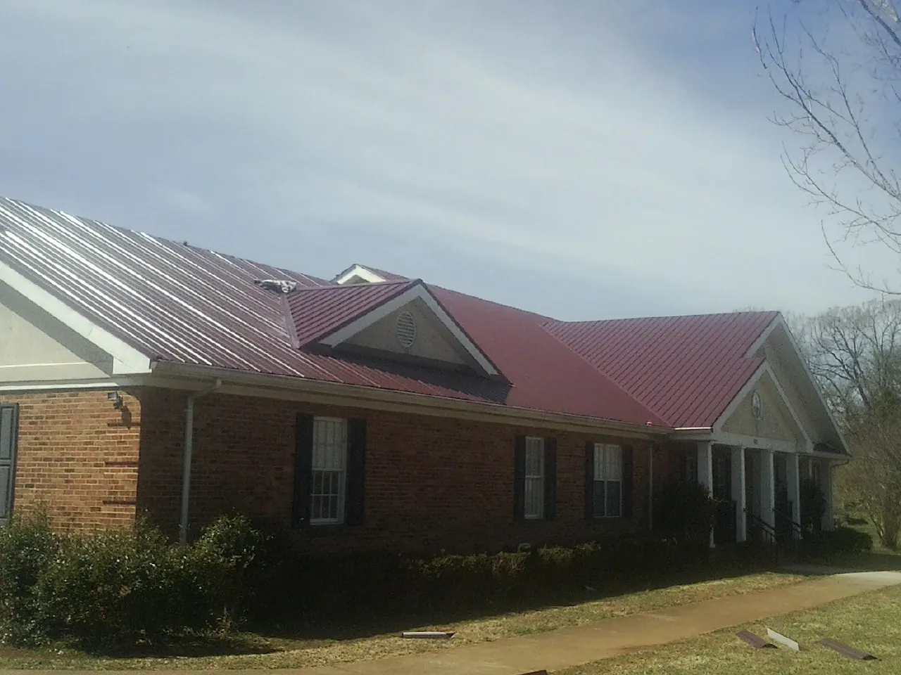 Red metal roof with gabled entries on a long brick building, from a Hail Damage Roof Repair job in Dayville