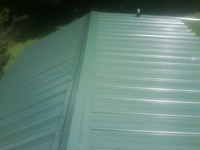 New green metal panels meeting at the ridge of a roof — Flat Roof Repair work by our crew in Dayville
