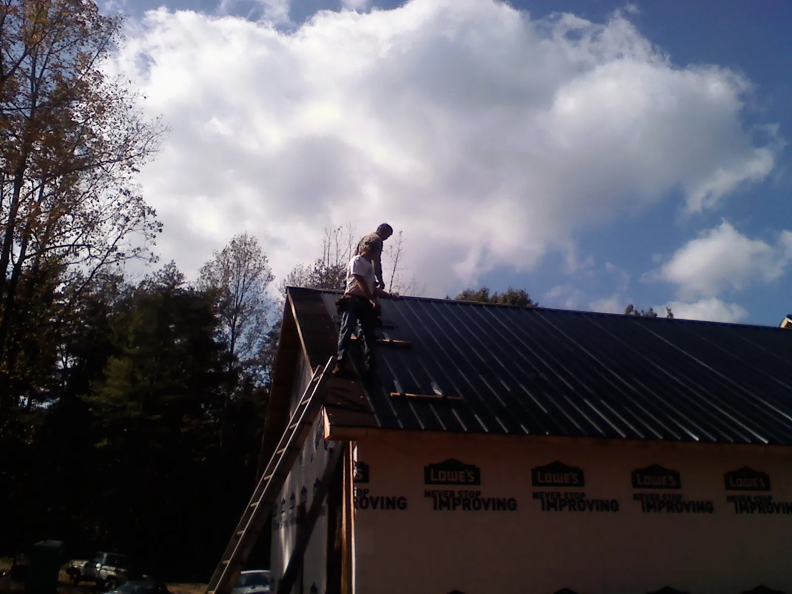 Roofer fastening dark metal panels high against a cloudy sky, from a Roof Inspection job in Dayville