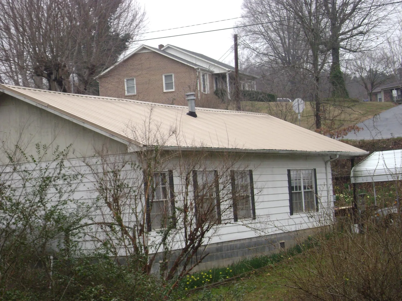 Tan metal roof on a white sided house set into a hillside — Commercial Roofing by Roofing Brothers in Dayville